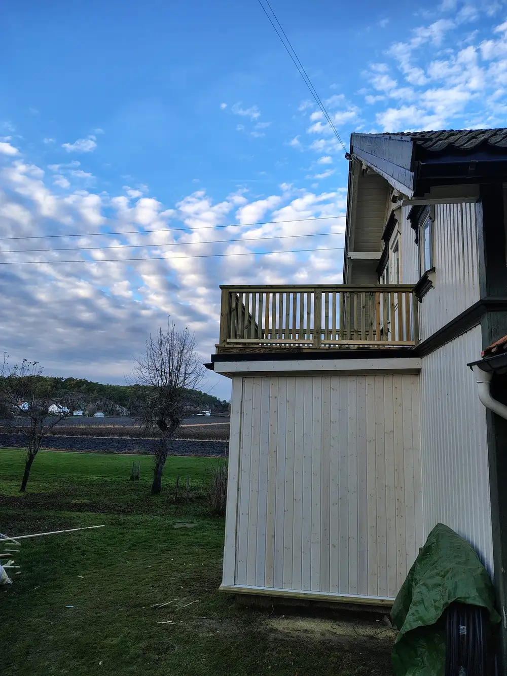 Husvegg med ny kledning og balkong, under en himmel med små skyer