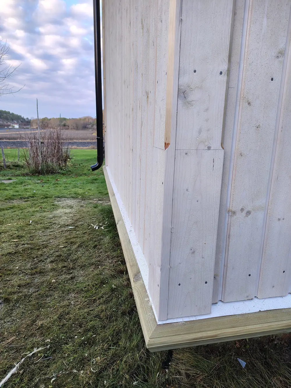 Lang vegg med ny stående kledning mot et jorde