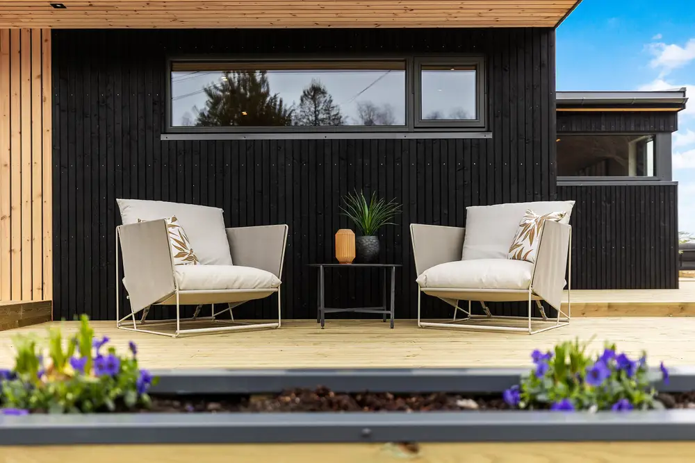 To stoler på en terrasse i tre foran sort kledning og et vindu