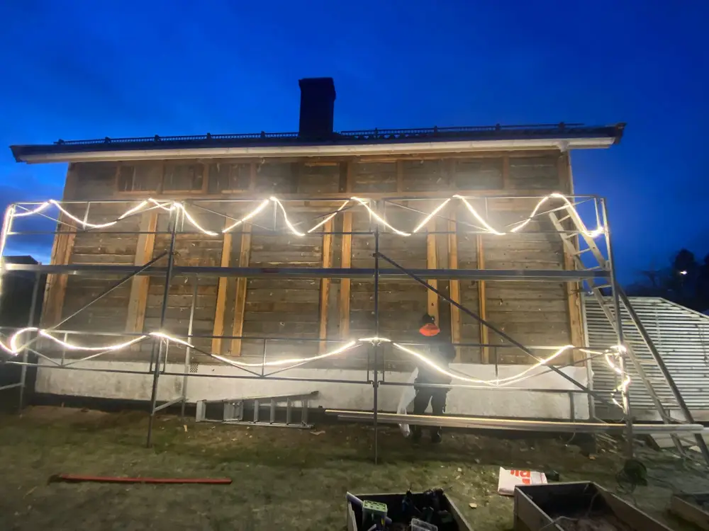 Hus med stillas i mørket, lyssatt med arbeidslys langs stillaset