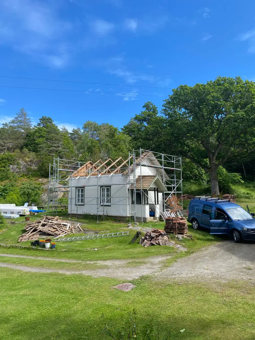 Hvitt eldre hus med stillas rundt og taket under arbeid, med bil og materialer foran